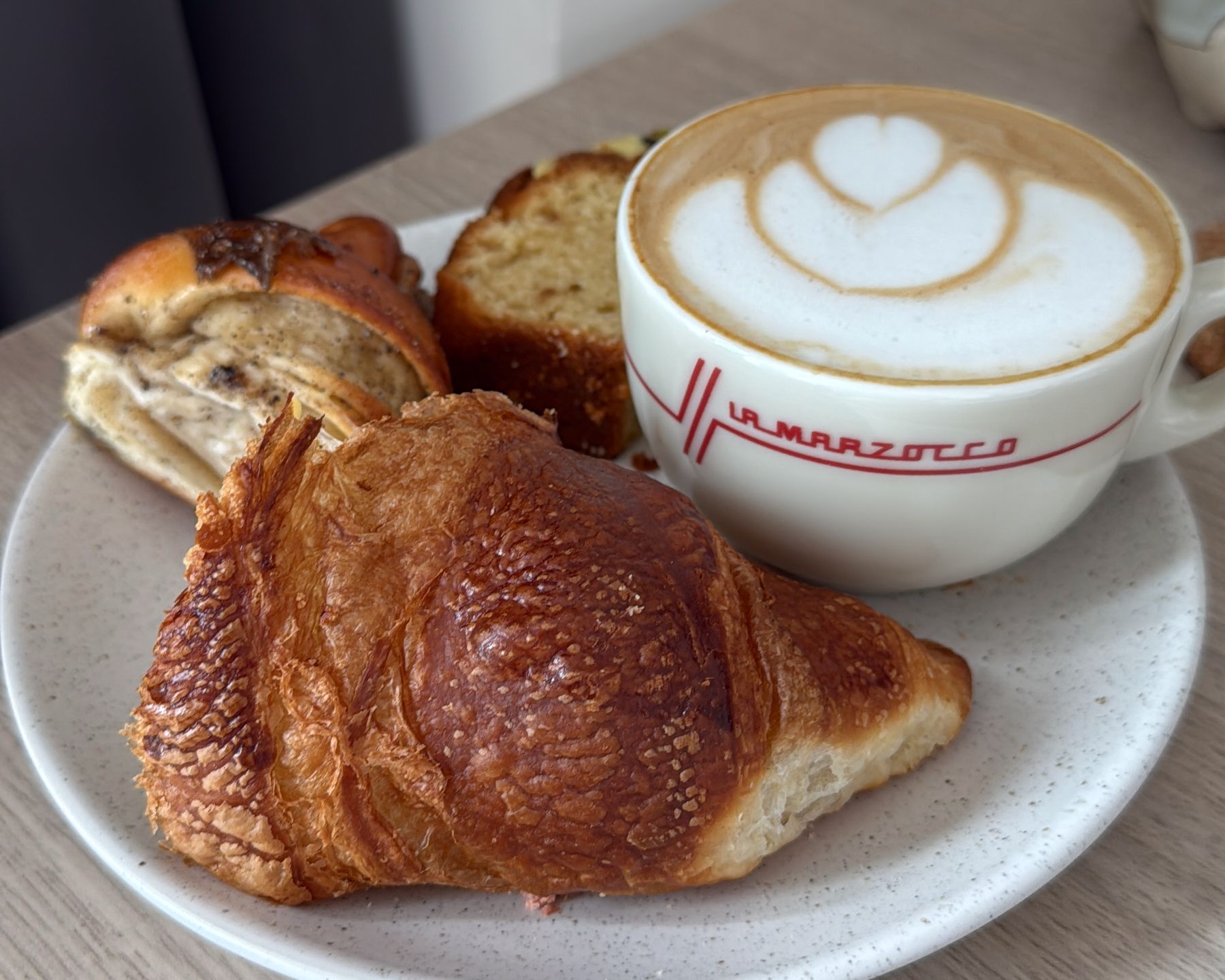 Oat cappuccino accompanied by a croissant, pistache cake and a cardamom roll